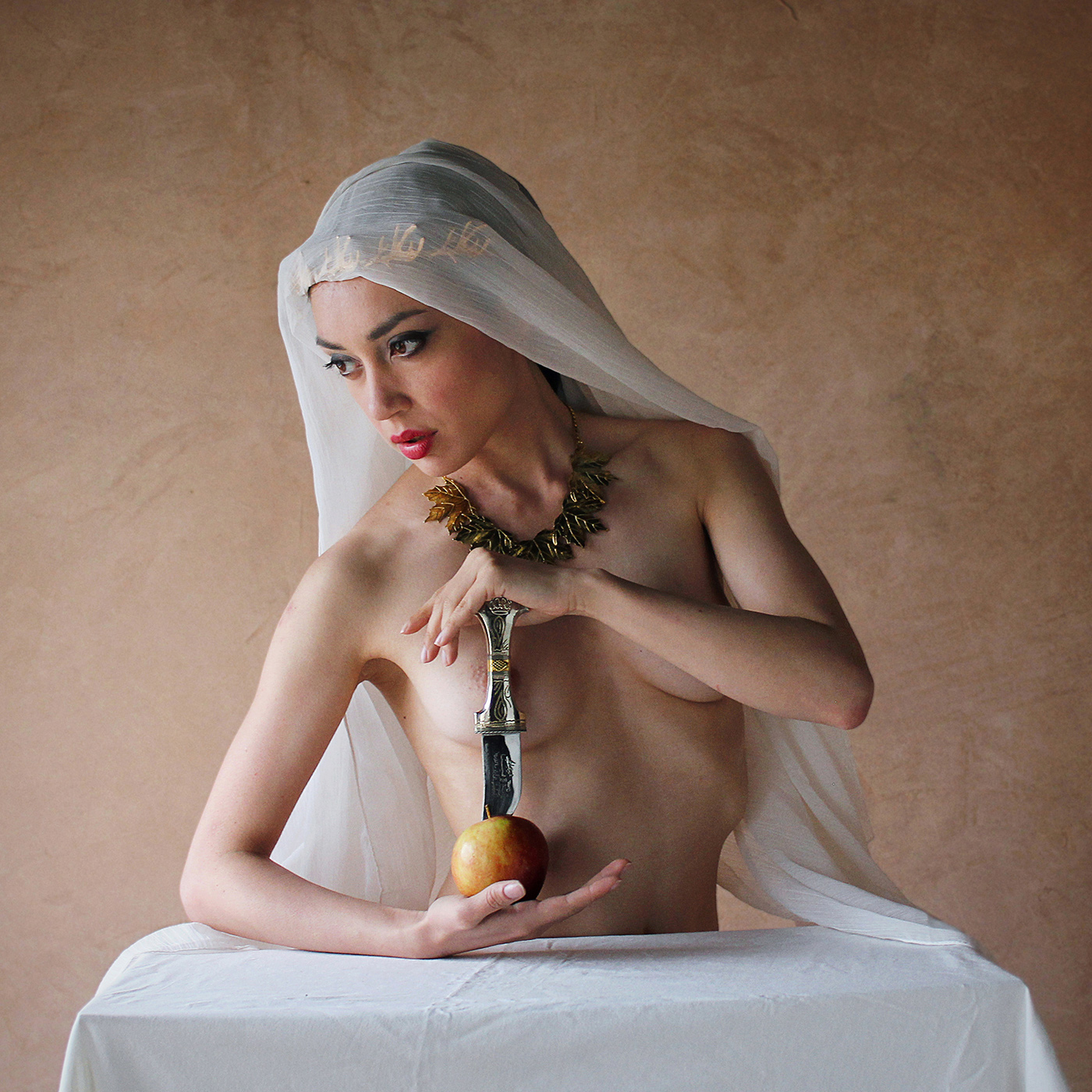 Artistic semi-nude photo. Veiled woman with a gold necklace holds a Jordanian dagger and an apple. Textured wall backdrop, natural light. Exudes exotic desert ambiance. veiled seduction, artistic nude, nude photography, nude photo, nude photo print, nude art photo, female nude art, Fine art nude photography, Elegant nude photography, Artistic nude portraits, Creative nude photography, Sensual artistic nudes, Artistic nude poses, Conceptual nude art, Romantic nude photography, Graceful nude portraits