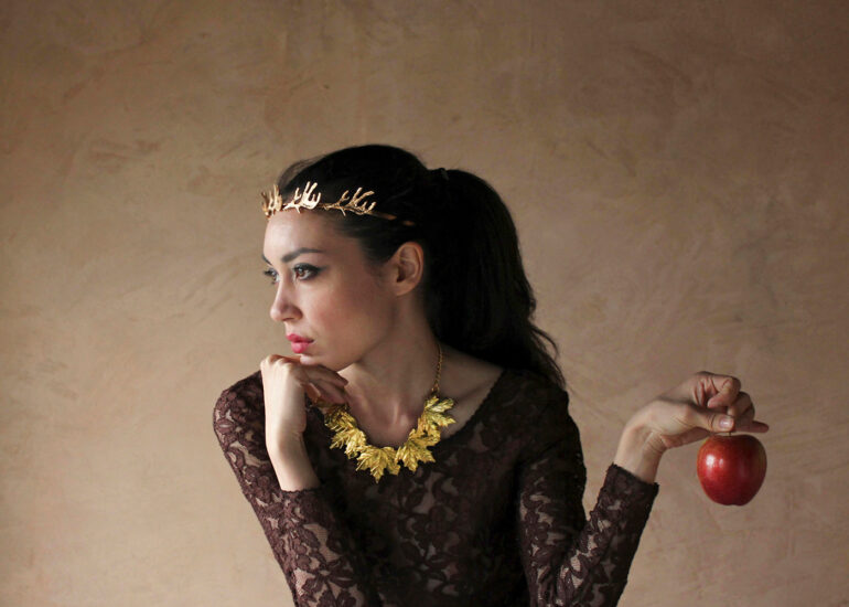 Conceptual fine art portrait of a woman wearing a crown and holding an apple, evoking power, elegance, and symbolic authority.