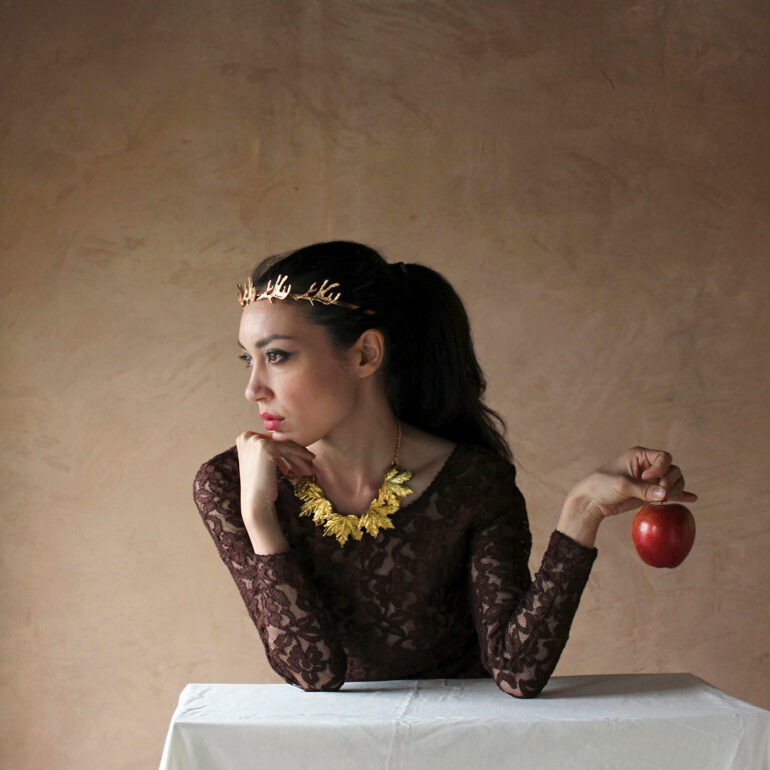Conceptual fine art portrait of a woman wearing a crown and holding an apple, evoking power, elegance, and symbolic authority.