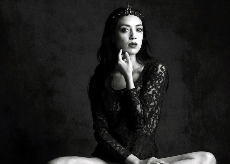 Black and white fine art portrait of a crowned woman seated in a composed pose, conveying authority, stillness, and strength.